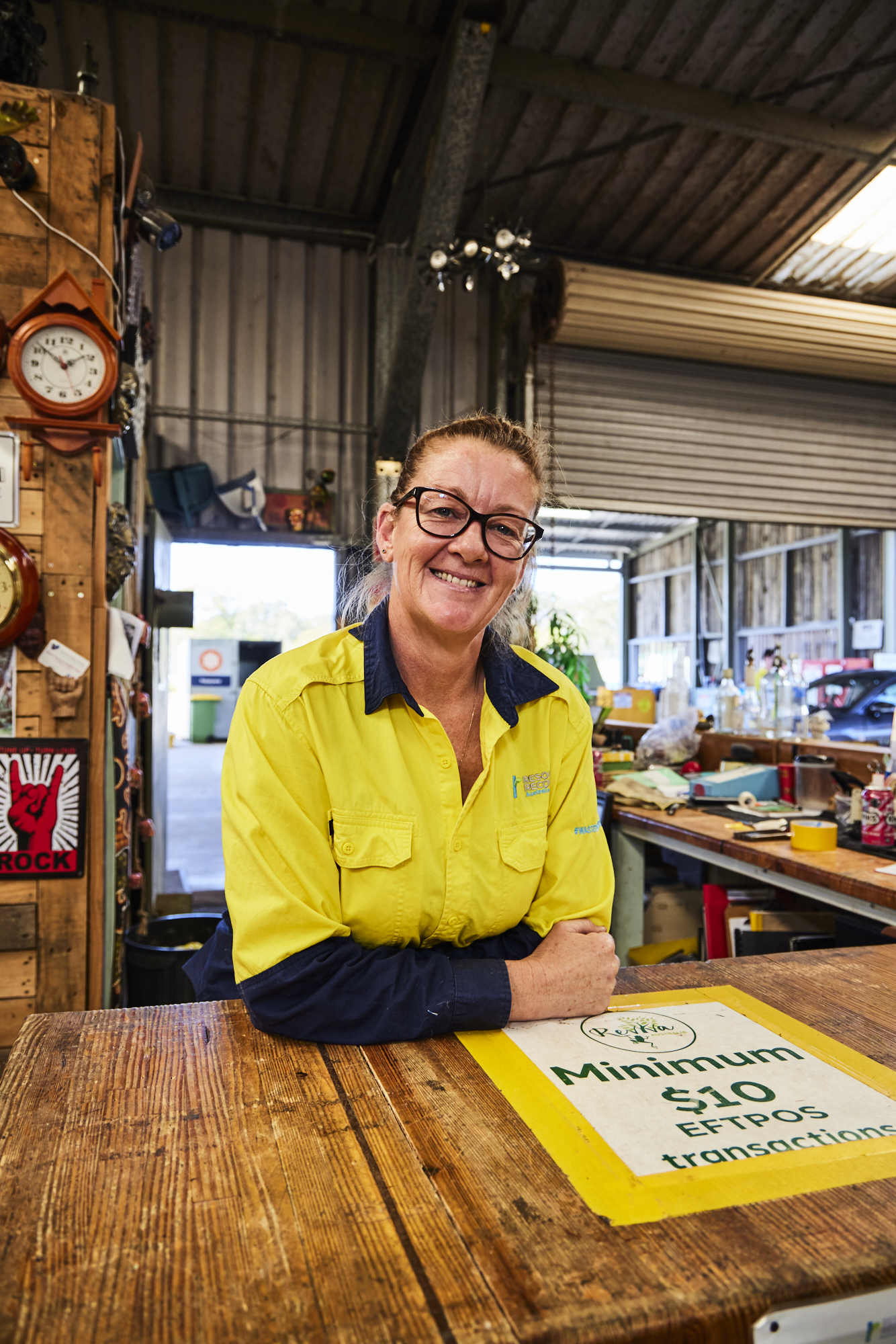 20240904_CR_FPL_1070 Female staff wearing the Resource Recovery uniform holding second hand items and standing in front of a shelf with second hand electrical equioment