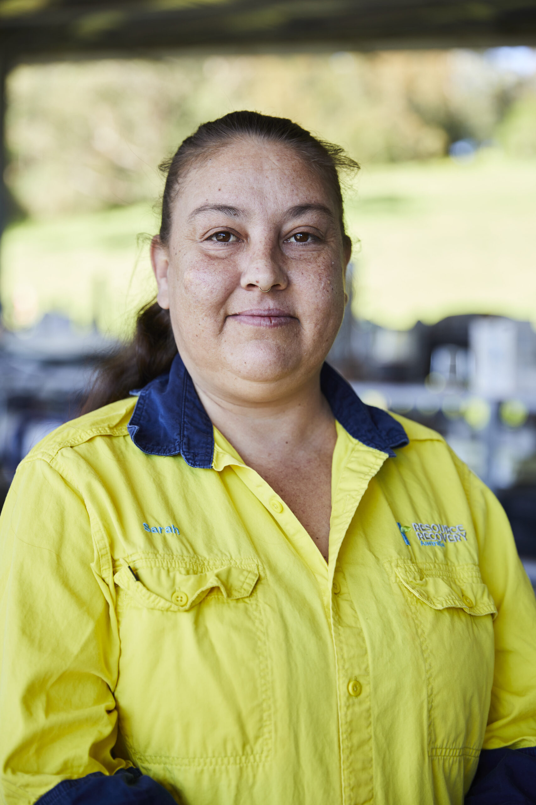 Female staff wearing the Resource Recovery uniform holding second hand items and standing in front of a shelf with second hand electrical equioment