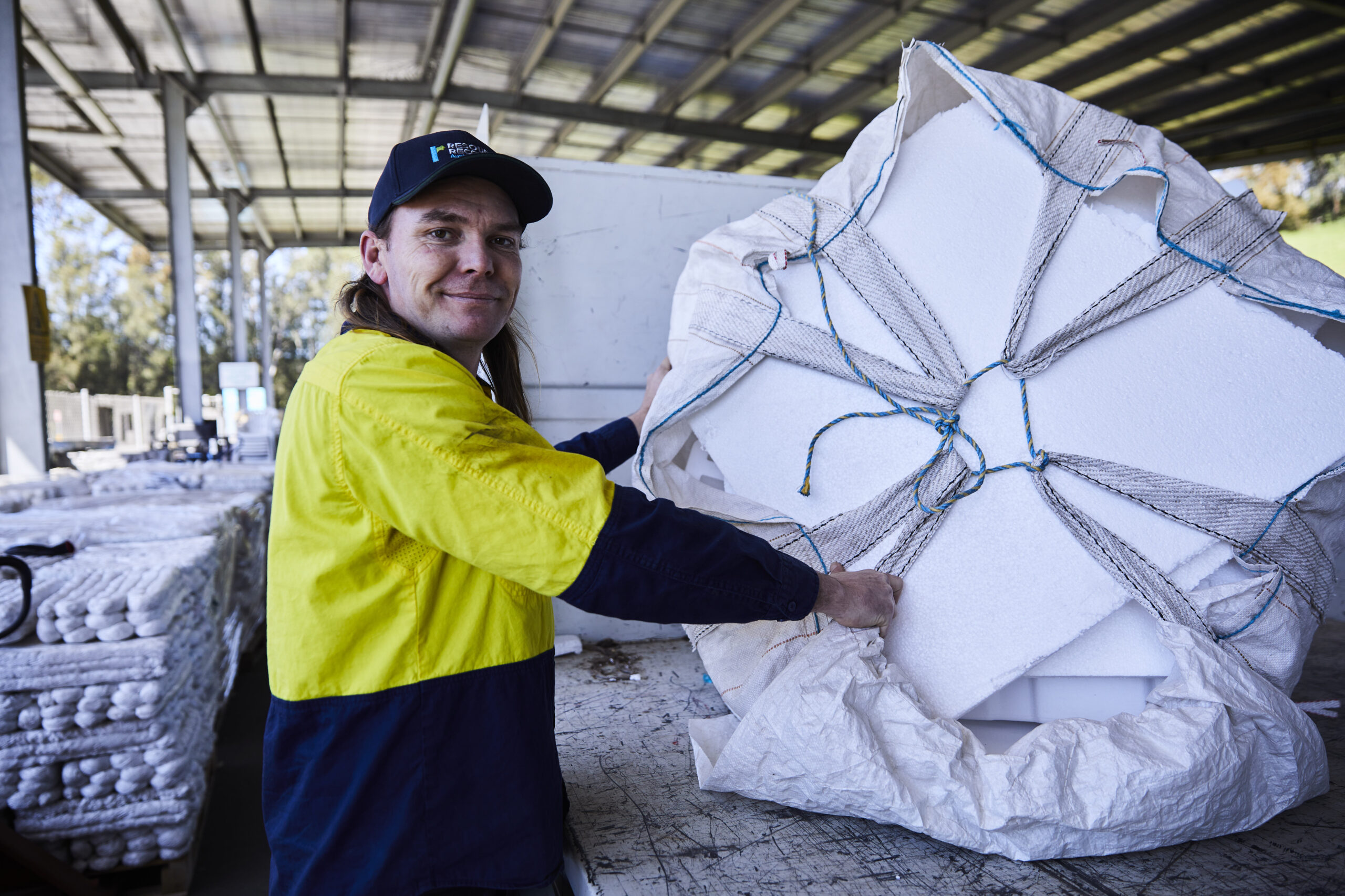 20250912_CR_FPL_0692 Female staff wearing the Resource Recovery uniform holding second hand items and standing in front of a shelf with second hand electrical equioment